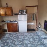 Self-catering room with a bed, compact kitchenette, fridge, microwave and wooden cupboards in Newton Park accommodation.