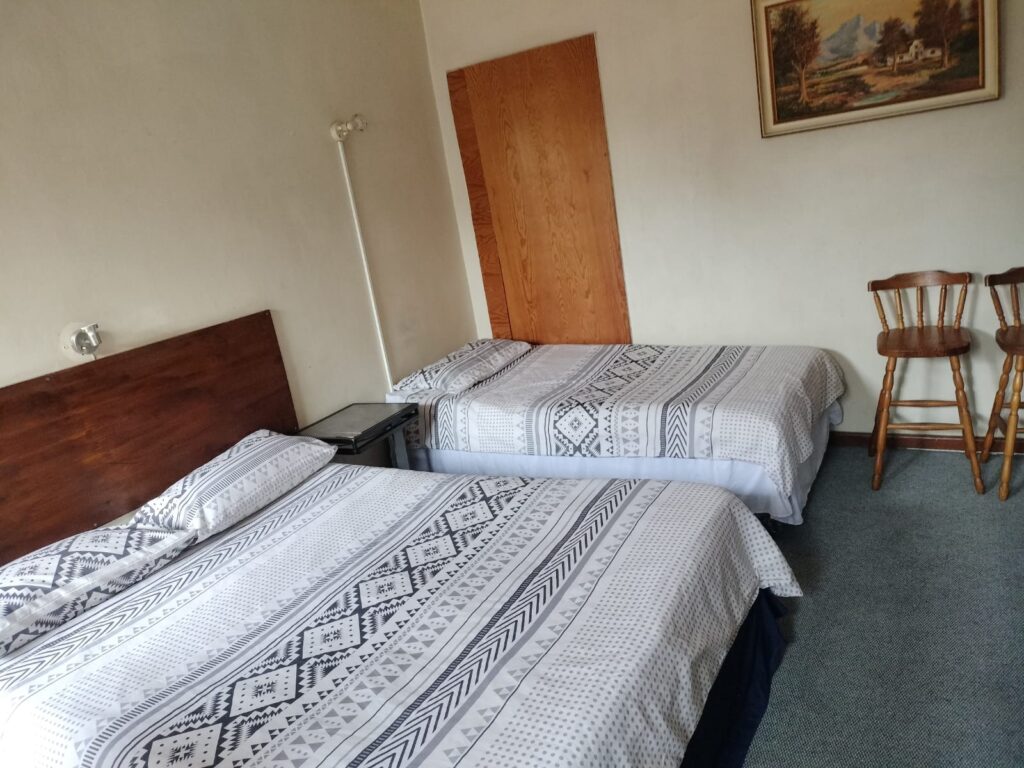 Bright bedroom with grey and white geometric bedding and built-in wooden cupboards at Newton Park accommodation.