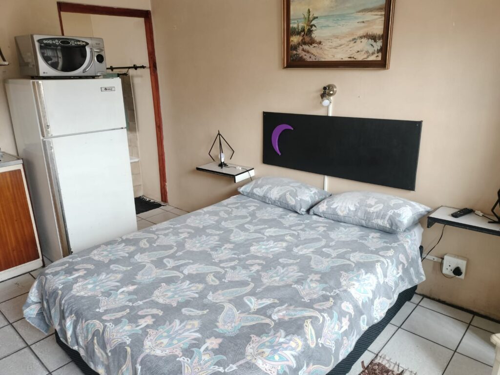 Neat bedroom with grey patterned bedding, a small fridge and kettle station in Newton Park accommodation.