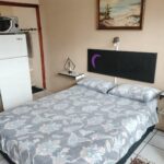 Neat bedroom with grey patterned bedding, a small fridge and kettle station in Newton Park accommodation.